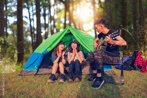 A group of Asian friends tourist drinking and playing guitar together with happiness in Summer while having camping