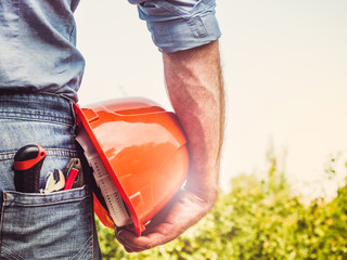 Handsome man with tools, standing against a background of green trees and the rays of the setting sun. View from the back, close-up. Concept of work and employment