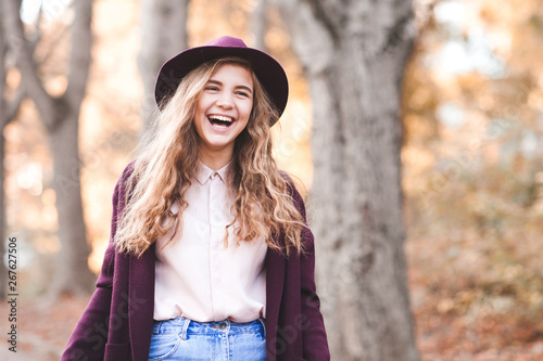 Laughing teen girl 14-16 year old wearing hat and jacket walking in park. Looking at camera. Teenagerhood.