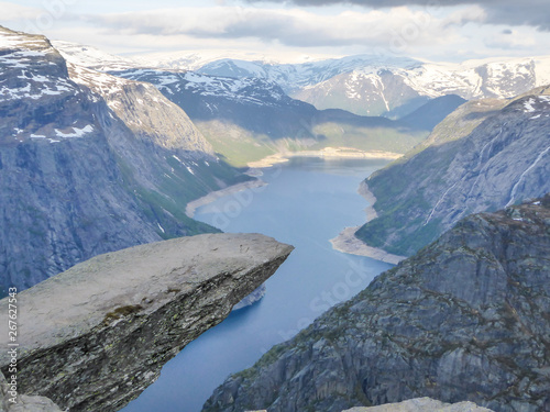 Famous rock formation  Trolltunga with a view from the above on Ringedalsvatnet lake  Norway. Rock hanging. Slopes of the mountains are partially covered with snow. The water of the lake is navy blue.