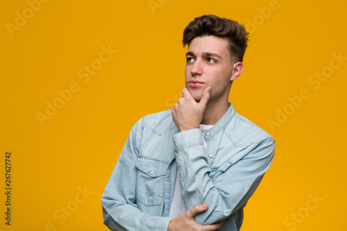 Young handsome student wearing a denim shirt looking sideways with doubtful and skeptical expression.
