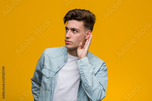 Young handsome student wearing a denim shirt trying to listening a gossip.