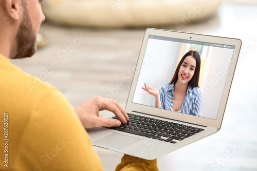 Young man using video chat on laptop at home, closeup. Space for design