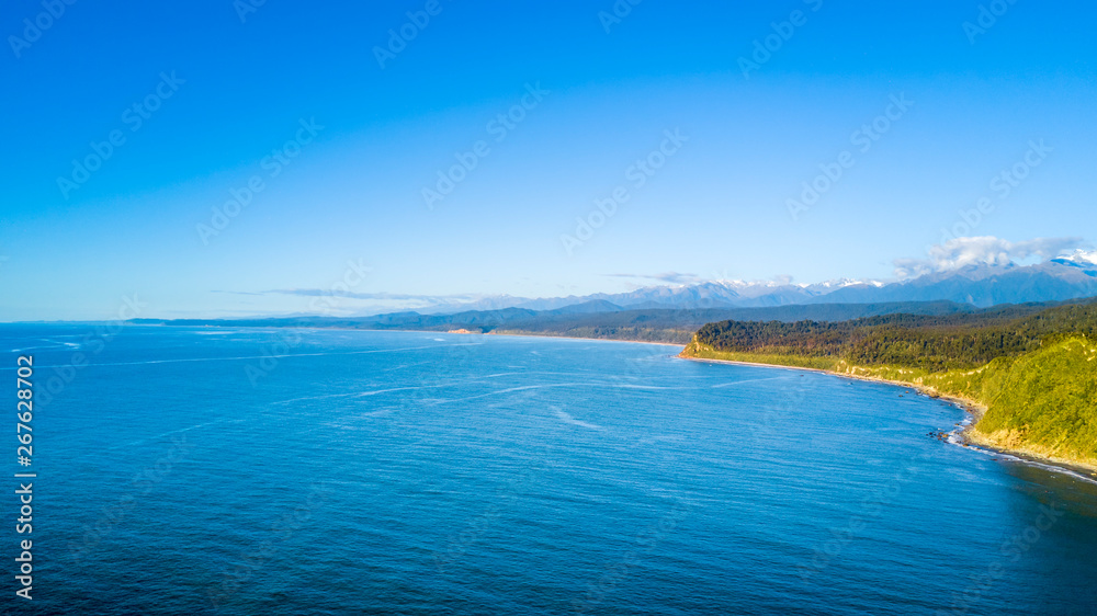 Ocean bay on a sunny day with green peninsula on the background. West Coast, South Island, New Zealand