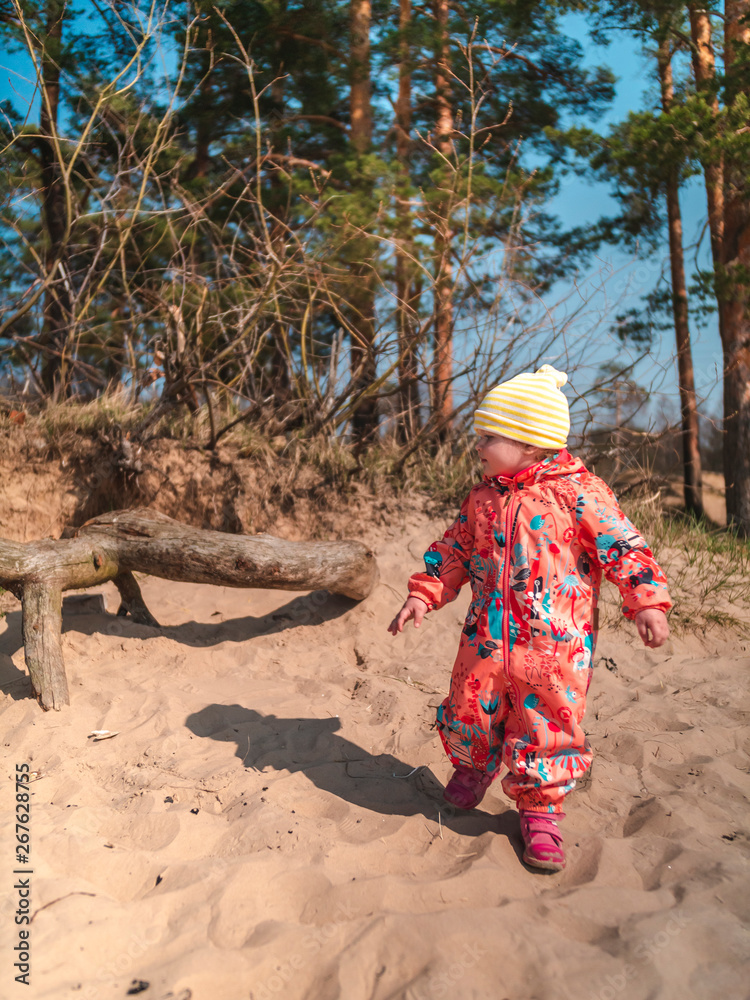 Little girl child in a coral suit walks on a sandy beach under the sun. The baby in a coral-pink suit plays on the beach Little girl child in a coral suit walks on a sandy beach under the sun. The baby in a coral-pink suit plays on the beach