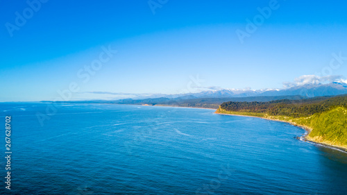 Ocean bay on a sunny day with green peninsula on the background. West Coast, South Island, New Zealand