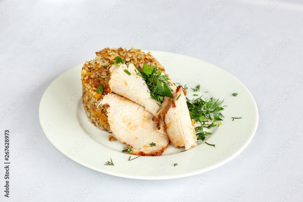 Chicken breast, buckwheat salad with greens on a white plate.
