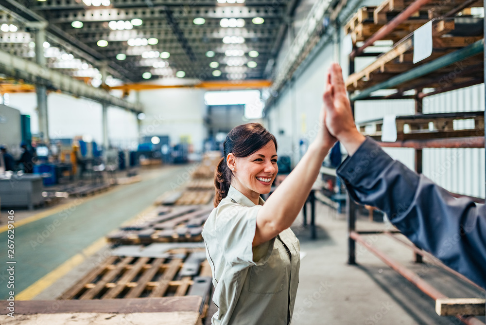 Female engineer high five with colleague at factory hall.