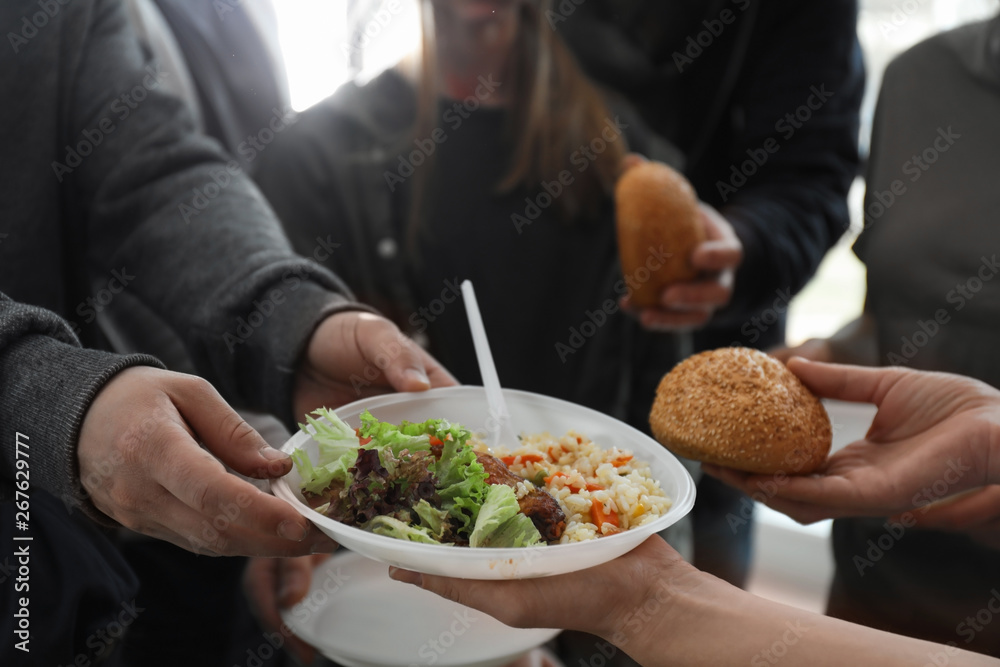 Poor man receiving food from volunteer indoors, closeup Poor man receiving food from volunteer indoors, closeup