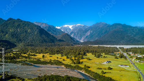 River running through the sunny valley with high mountains on the background. West Coast, South Island, New Zealand
