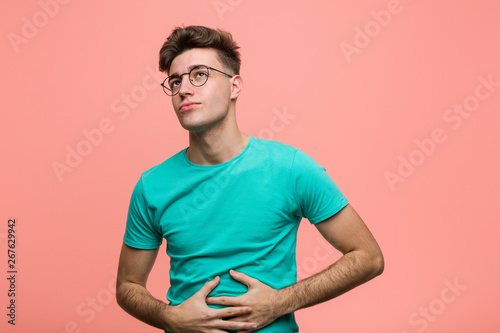 Young cool caucasian man touches tummy, smiles gently, eating and satisfaction concept. © Asier