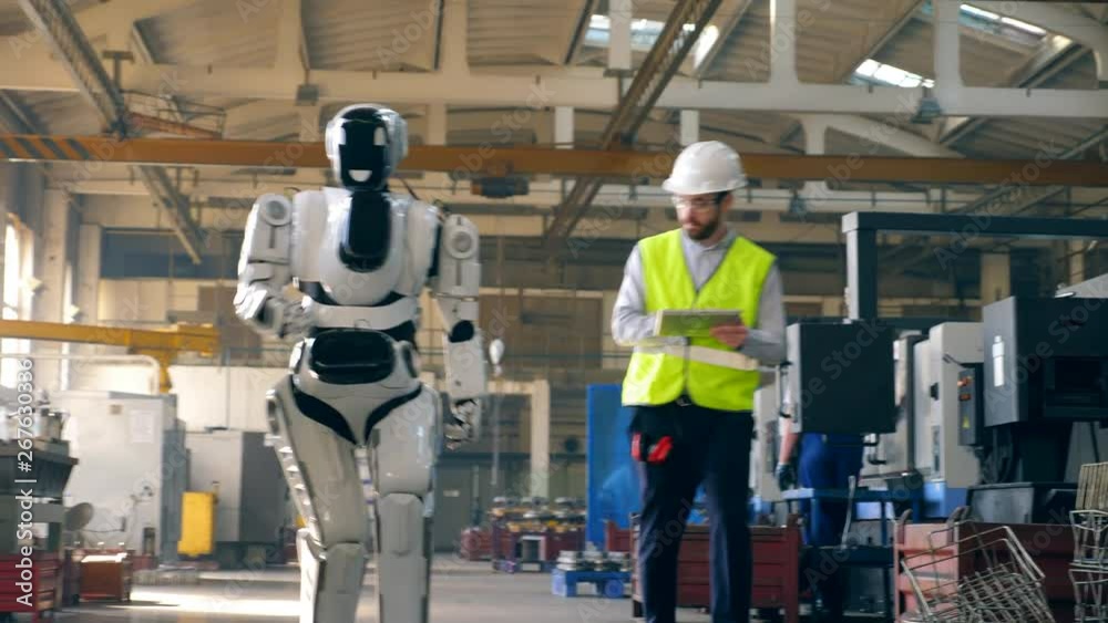 Robot is walking along the factory under control of a male specialist