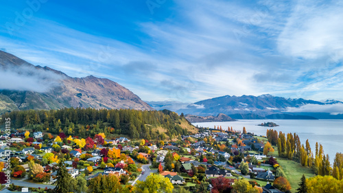 Small town surrounded by yellow autumn trees on a shore of pristine lake with mountains on the background. Wanaka, Otago, South Island, New Zealand photo