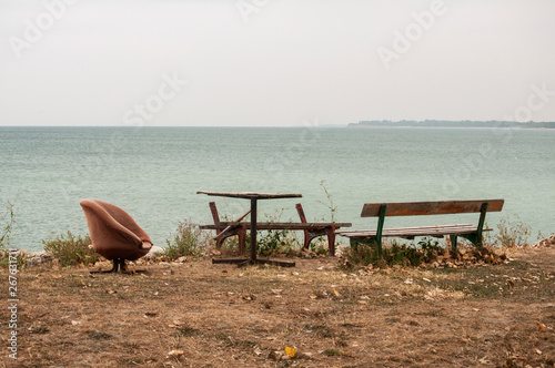 Lonely empty wooden obsolete vintage bench and chair on the seashore