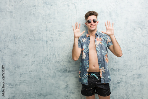Young caucasian man wearing a swimsuit showing number ten with hands.