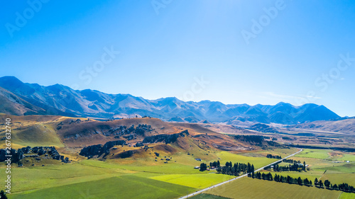 Road running through farmland with mountains on the background. West Coast, South Island, New Zealand