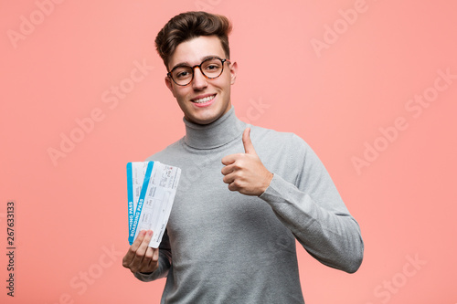 Young cool man holding an air tickets smiling and raising thumb up