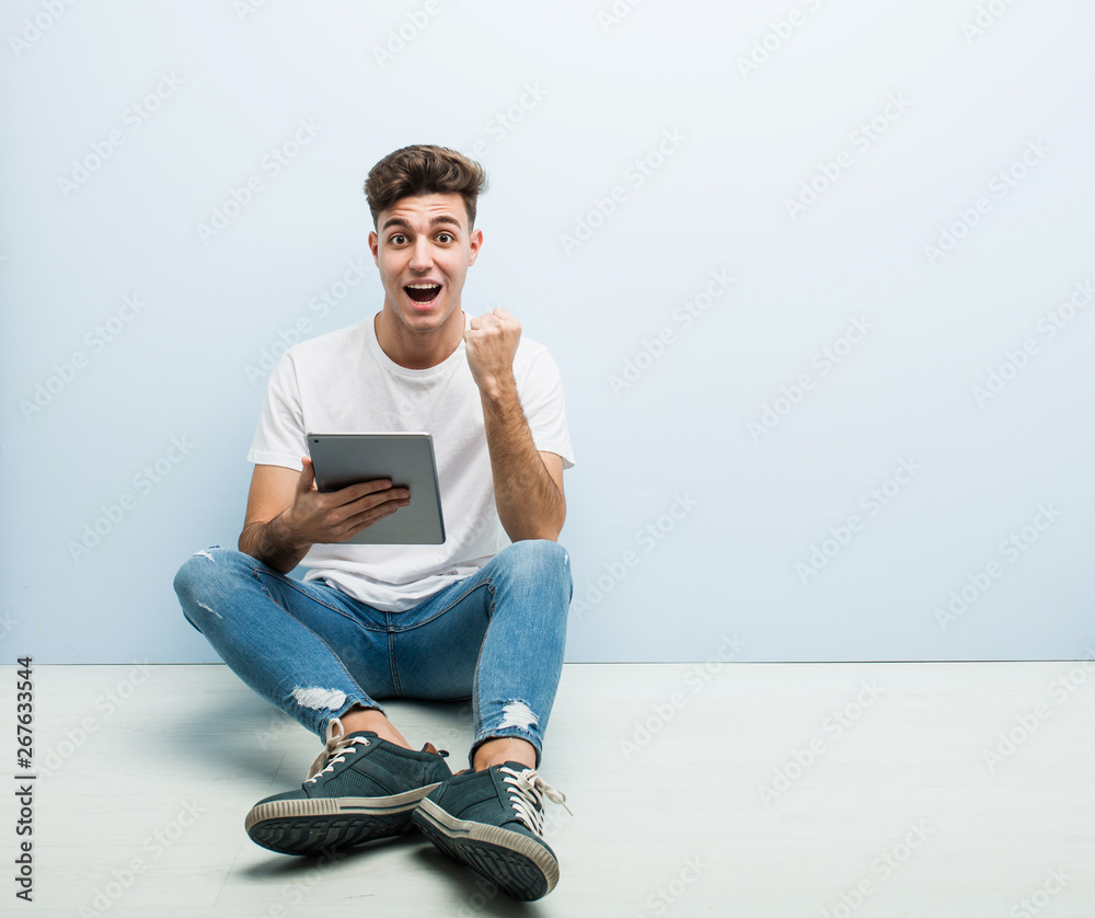 Young man holding a tablet sitting indoor cheering carefree and excited. Victory concept. Young man holding a tablet sitting indoor cheering carefree and excited. Victory concept.
