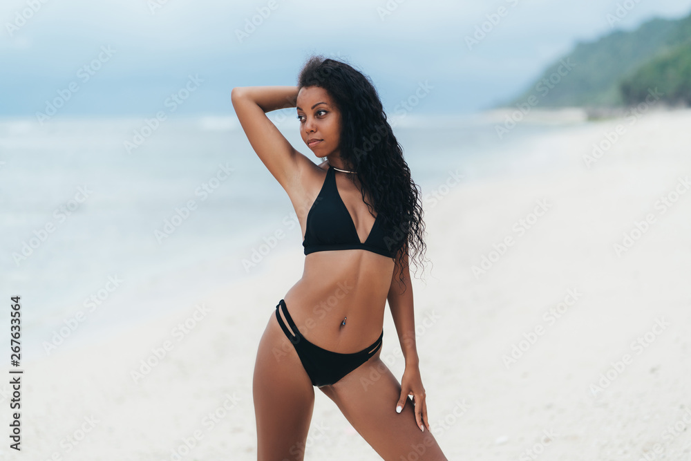 Beautiful sexy dark skinned girl in swimwear posing on white sand beach, Afro american woman resting on paradise island