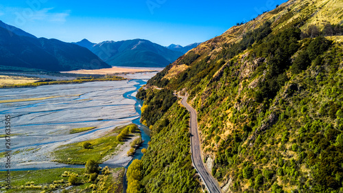 Road running on the rocky cliff along a river with mountains on the background. West Coast, South Island, New Zealand