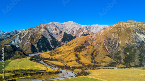 River running across farmland with mountains on the background. West Coast, South Island, New Zealand.