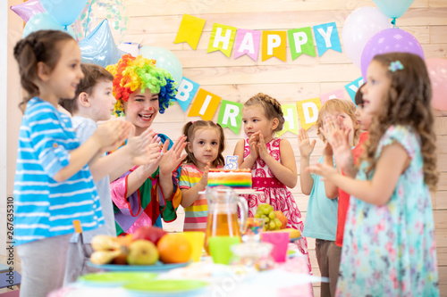 Childs are happy after they have blowed candles out on birthday party. Kids with clown clap their hands