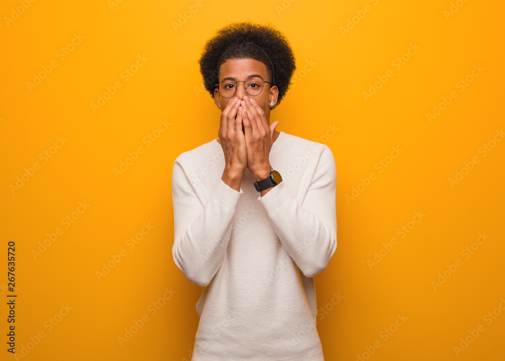 Young african american man over an orange wall very scared and afraid hidden Young african american man over an orange wall very scared and afraid hidden