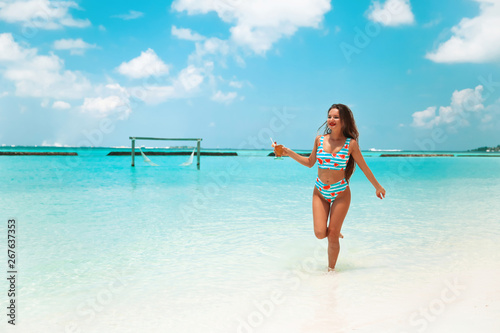 Carefree bikini Woman on tropical beach. Pretty slim girl with coctail enjoying on exotic island in turquoise ocean. Brunette model in trendy swimwear having fun in Maldives lagoon.