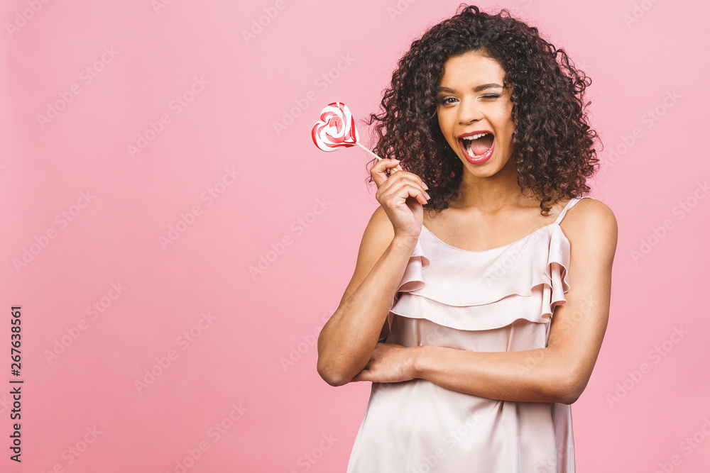 Happy sexy american afro girl eating lollipop. Beauty glamour model woman holding pink sweet colorful lollipop candy, isolated on pink background. Sweets. Happy sexy american afro girl eating lollipop. Beauty glamour model woman holding pink sweet colorful lollipop candy, isolated on pink background. Sweets.