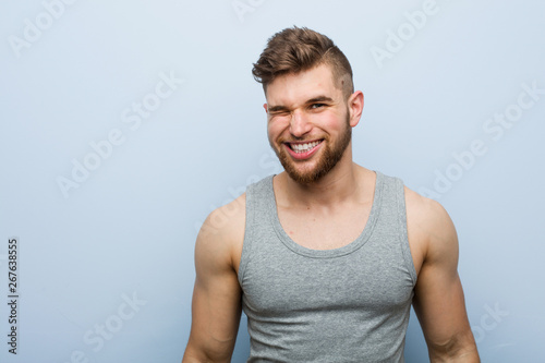 Young handsome fitness man winking, funny, friendly and carefree.