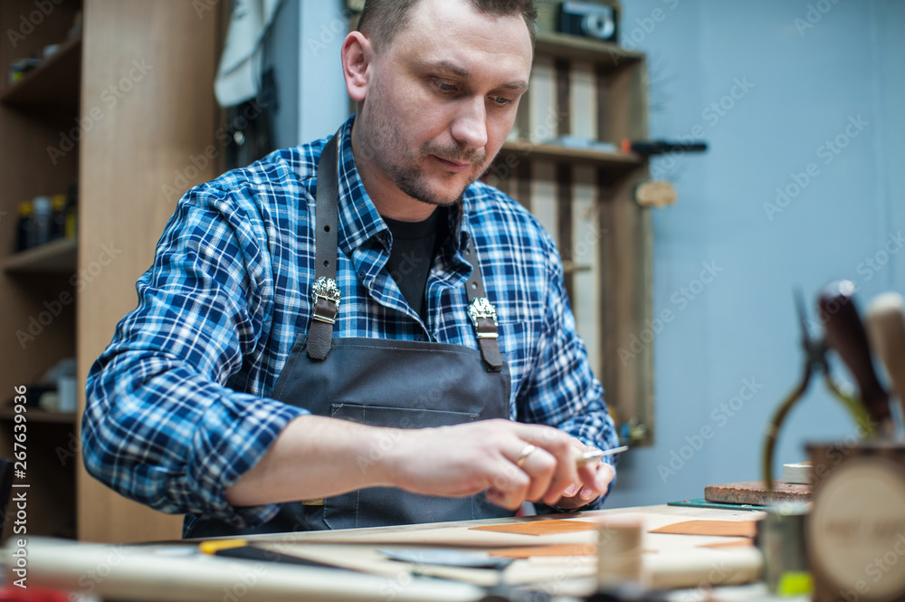 Man working with leather textile at a workshop. Craftman cutting leather. Concept of handmade craft production of leather goods. Man working with leather textile at a workshop. Craftman cutting leather. Concept of handmade craft production of leather goods.