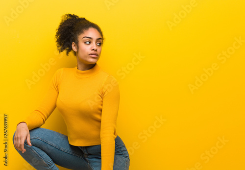 Young black woman sitting over an orange wall © Asier