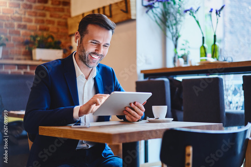 Businessman sitting in cafe using tablet and talking through wireless headphones photo