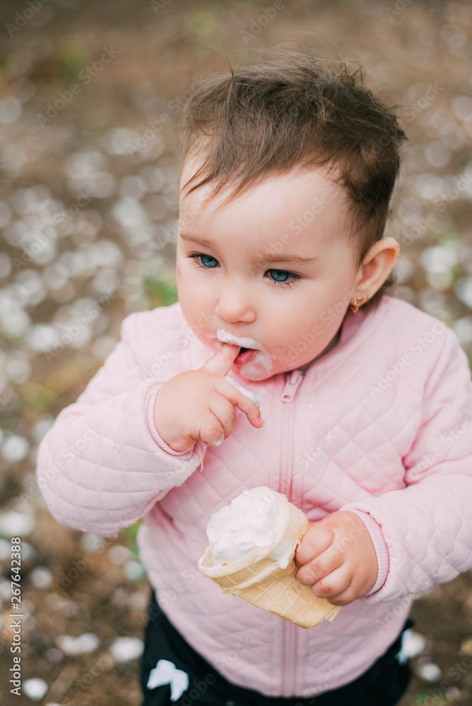 little girl in the garden on the background of greenery and trees very cute eating ice cream finger in a waffle Cup little girl in the garden on the background of greenery and trees very cute eating ice cream finger in a waffle Cup