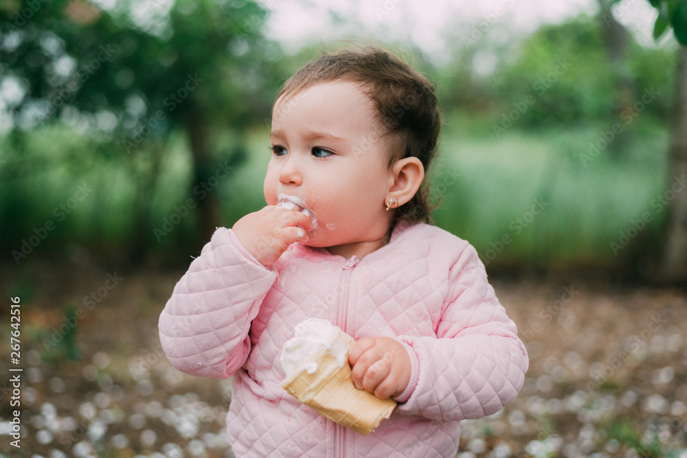 little girl in the garden on the background of greenery and trees very cute eating ice cream finger in a waffle Cup little girl in the garden on the background of greenery and trees very cute eating ice cream finger in a waffle Cup