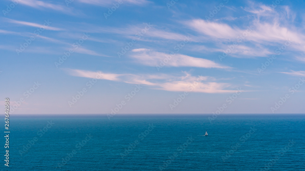 Seascape background with a sailboat navigating on a blue calm sea. 