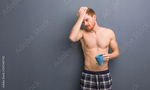 Young shirtless redhead man worried and overwhelmed. He is holding a coffee mug.