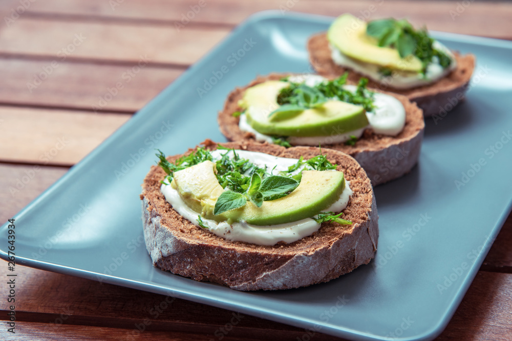 Sandwiches with avocado, sour cream and greens on a gray plate on a wooden table Sandwiches with avocado, sour cream and greens on a gray plate on a wooden table
