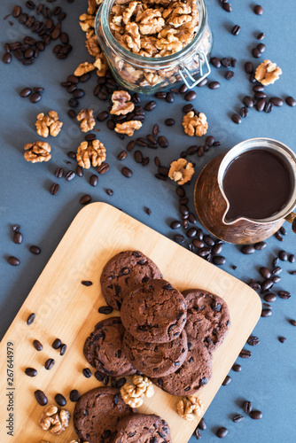 Freshly made coffee in old rustic Turkish coffee pot on dark background with coffee beans, chocolate cookies, sugar and walnuts – view with copy space. Aroma beverage drink. Flat lay
