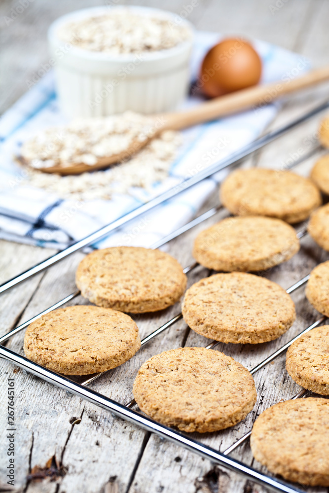 Baking grid with fresh oat cookies on rustic wooden table background, ingredients and kitchen utensil closeup. Baking grid with fresh oat cookies on rustic wooden table background, ingredients and kitchen utensil closeup.