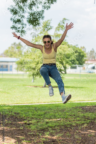 Female teen with pretty face jumping for joy while laughing out loud at grassy park.