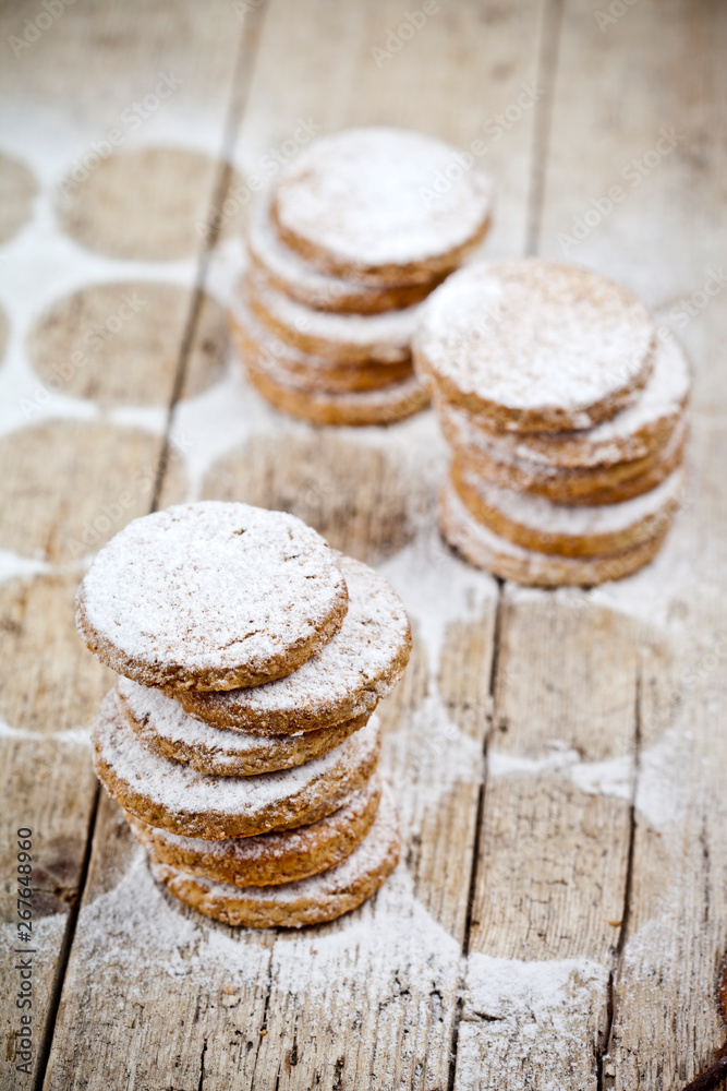 Fresh oat cookies stacks with sugar powder on rustic wooden table.