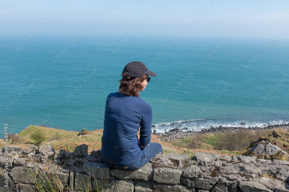 Woman looking at ocean back to camera, sunny day