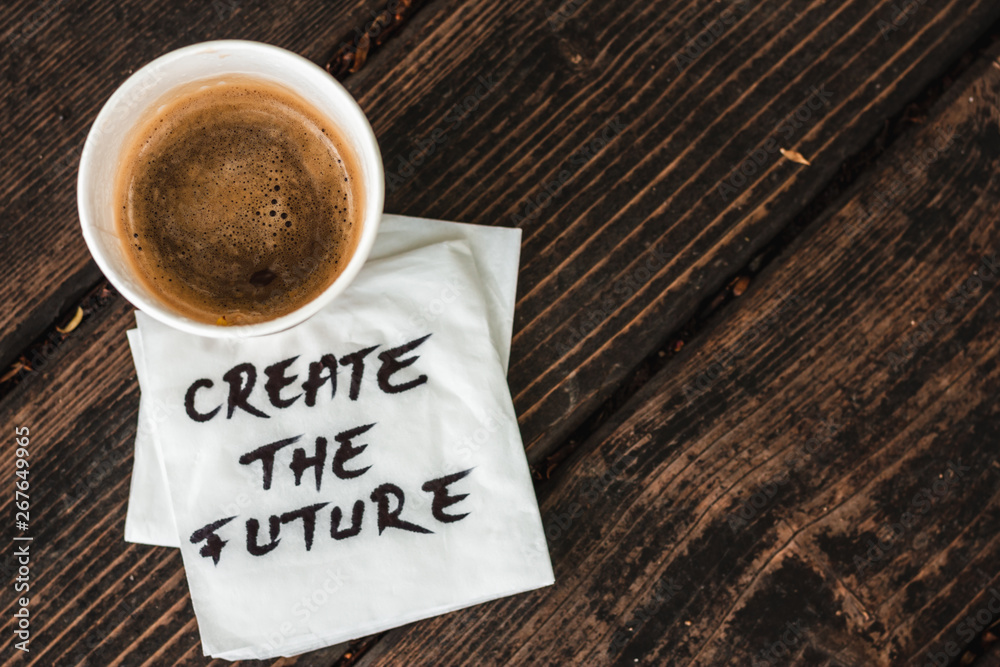 Full cup of coffee with foam sitting on white napkin with the message create the future hand written on it placed on a wooden surface – Concept image for inspirational messages Full cup of coffee with foam sitting on white napkin with the message create the future hand written on it placed on a wooden surface – Concept image for inspirational messages