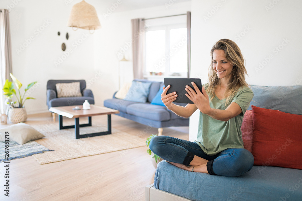 Happy woman relaxing on couch at home using tablet Happy woman relaxing on couch at home using tablet