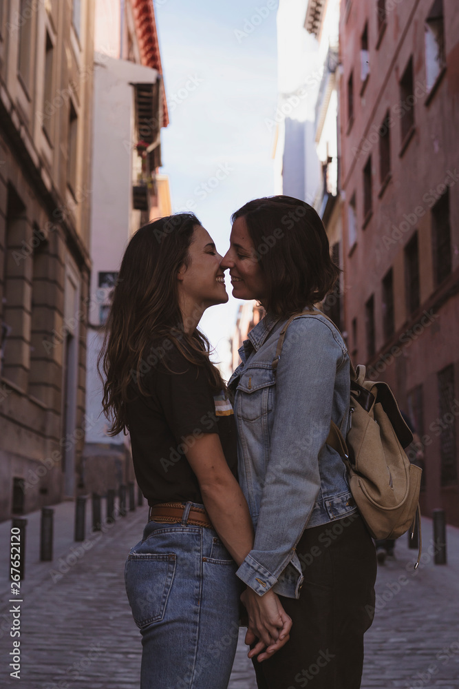 Attractive young women lesbian couple kissing and smiling in a street of Madrid.
