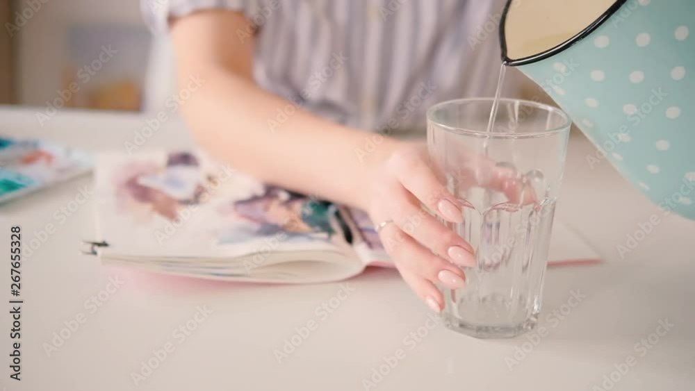 Artist painting. Delicate female hands pouring water from jug into glass. Desk, open watercolor sketchbook on. Inspiration. Artist painting. Delicate female hands pouring water from jug into glass. Desk, open watercolor sketchbook on. Inspiration.