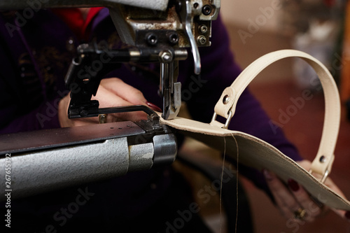 A woman sews a leather strip with a special sewing machine for leather, used in the production of handbags /shoes