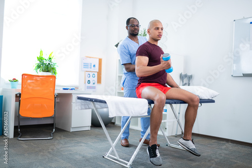 Bodybuilder in sports clothes exercising his arms visiting therapist