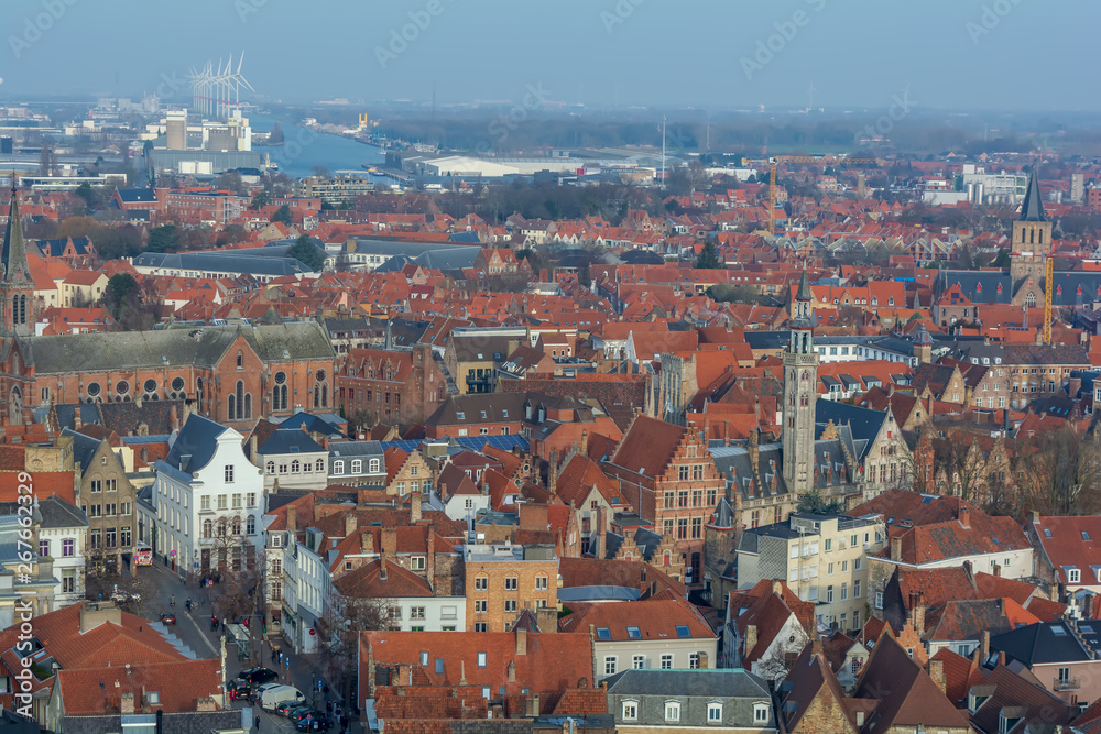 Fantastic Bruges city skyline with red tiled roofs, The Poortersloge (Burgher’s Lodge) tower and windmills in the background. View to Bruges medieval cityscape from the top of the Belfry Tower.